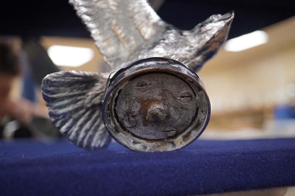 Two chrome car mascots, one in the form of an eagle stamped Finnigans London, wingspan 26cm, and the other of a classical child writing, mounted on a substantial radiator cap and oak base. Condition - fair to good, some